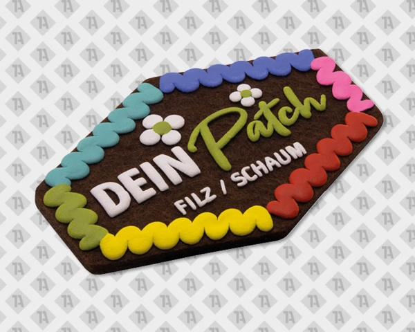 Hexagonaler Patch aus Filz mit farbigem Zickzack-Rand und Schrift „Dein Patch / Filz Schaum“.