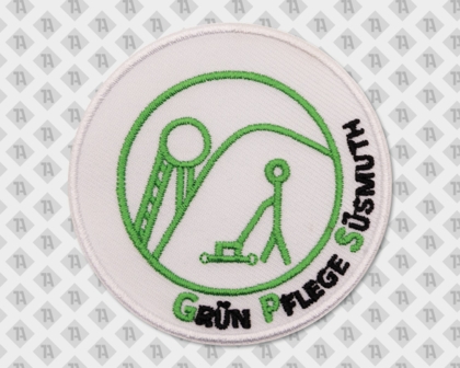 Runder Aufnäher mit grünem Logo und Schrift „Grün Pflege Süsmuth“, zeigt Figur mit Rasenmäher – Symbol für Garten- und Landschaftspflege.