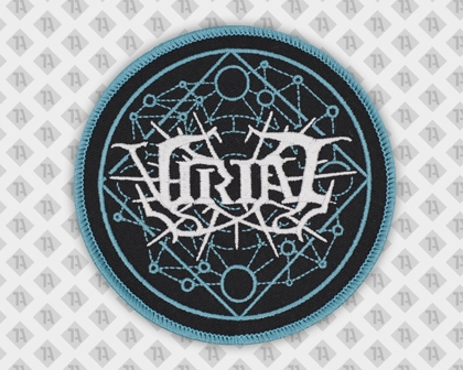 Runder Patch mit GRIM-Logo in Weiß auf geometrisch-blauem Muster mit türkisfarbenem Kettelrand