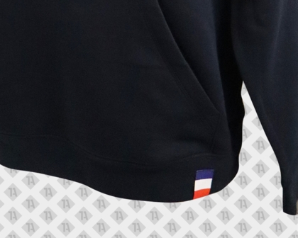 Schwarzer Hoodie mit blau-weiß-rotem Loopfold-Weblabel am Saum.