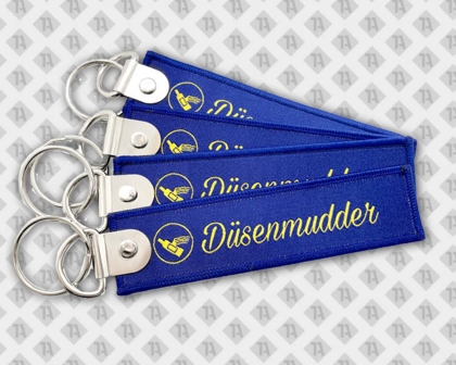 Blaue gewebte Schlüsselanhänger mit gelber Schrift „Düsenmudder“ und Metallverschluss.