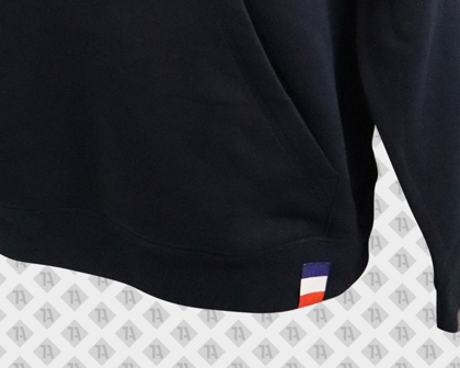 Schwarzer Hoodie mit blau-weiß-rotem Loopfold-Weblabel am Saum.