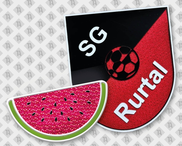 Ein Vereinswappen (schwarz/rot) und eine Melonenscheibe als 3D-Applikation auf Trägermaterial