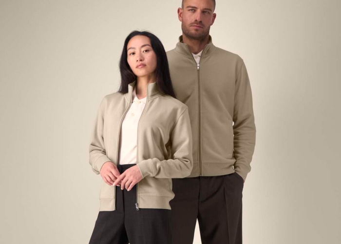 Lockiger junger Mann lacht im grauen Sweatshirt und fasst sich an den Kopf.