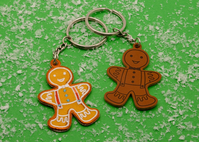 Zwei Schlüsselanhänger die ein Lebkuchenmännchen zeigen - einmal in gestickt und einmal aus Kunstleder - grüner Untergrund mit Kunstschnee