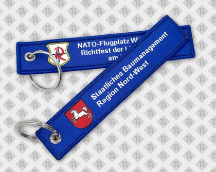 Blauer gewebter Schlüsselanhänger mit weißer Schrift, Wappen und Metallring.