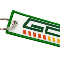 Weißer gewebter Schlüsselanhänger mit grünem Rand, mehrfarbigem Logo und Metallring.