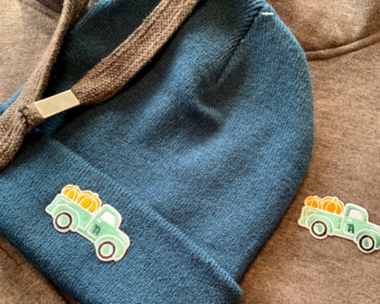 Blaue Beanie und brauner Hoodie mit gesticktem Patch eines grünen Trucks mit Kürbissen.