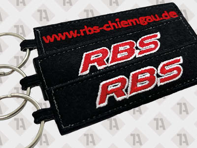 1A Schlüsselanhänger aus schwarzem Material mit roter und weißer Stickerei, personalisiert mit Logo und Webadresse