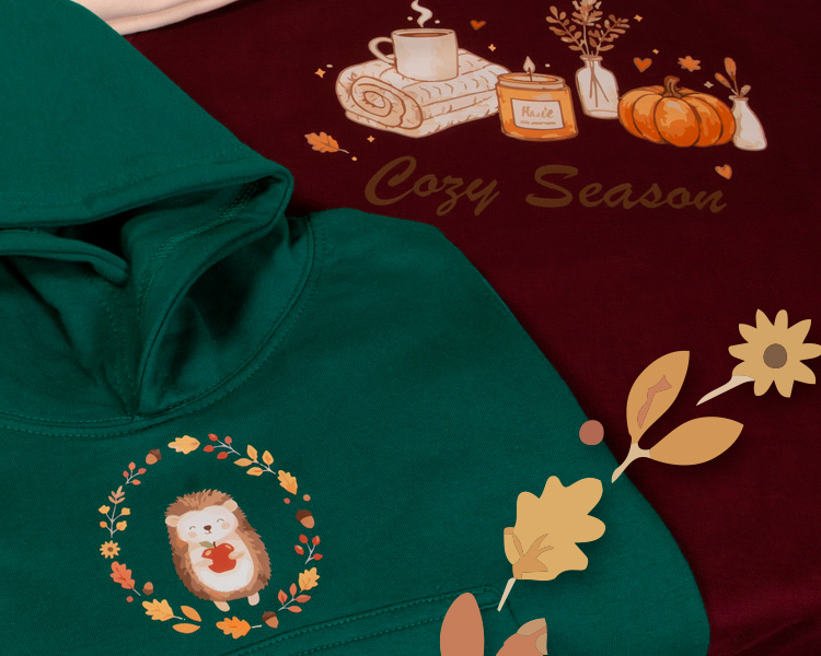 Zwei Motive in der Detailansicht der 1A-Herbstkollektion - Igel mit Jerbstkranz auf grünem Hoodie und "Cozy Season" auf dunkelrotem Shirt